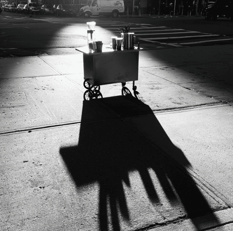 A Blue Bottle style cold brew cart sitting unused on a city sidewalk, representing the collapse of the brand’s mobile vending experiment.