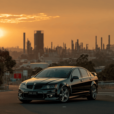 A Pontiac G8 GT driving on a wide American road with a faint outline of the Holden factory, symbolizing the Australian roots of Pontiac’s final performance sedan.