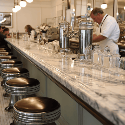 A vintage marble topped soda fountain counter with syrup bottles and chrome stools, representing the lost era of American soda fountains.