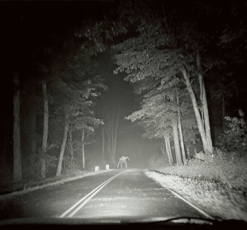 Dashcam-style scene showing a frog-like humanoid figure on a dark Ohio road, referencing the Loveland Frogman sighting