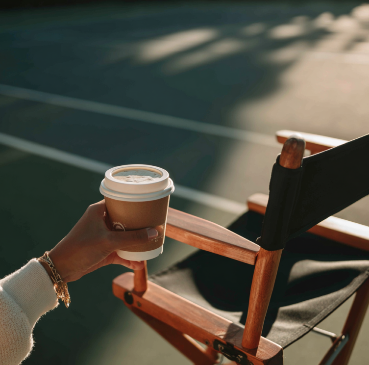 tennis judge’s hand holding coffee cup beside a line judge chair on an empty court, symbolizing scandal and accusation