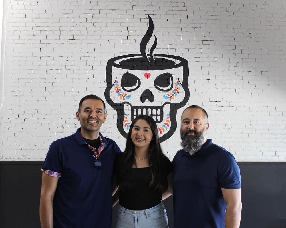 HeadCount coffee founders standing in front of a brick wall with the logo behind them